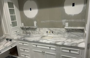 White marble countertop with built-in sink and white cabinetry in a bathroom under renovation.