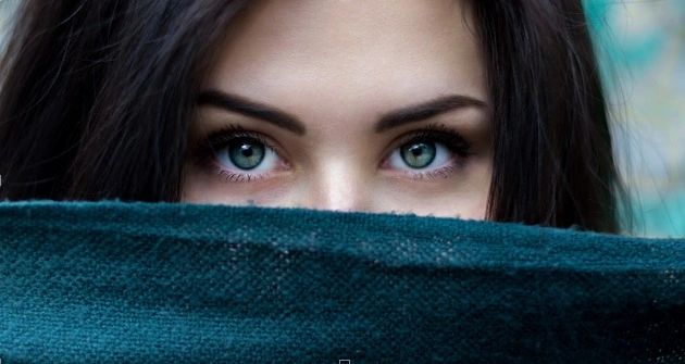 Close-up of a woman's striking blue-green eyes peeking over a dark teal fabric.