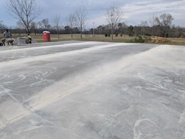 Freshly poured concrete slab drying outdoors with workers and a portable toilet nearby.