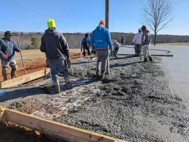 Workers pour and smooth concrete on a construction site under clear blue sky.