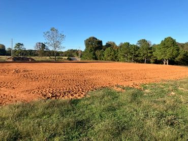 A large area of freshly tilled red soil under a clear blue sky.