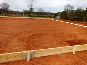Cleared red dirt construction site framed with wooden boards.