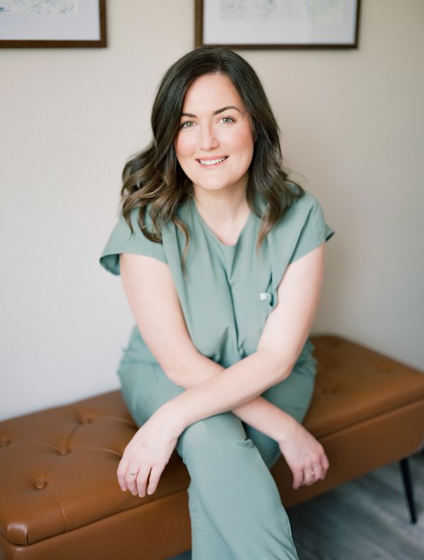 Smiling woman in green scrubs sitting on a brown bench.