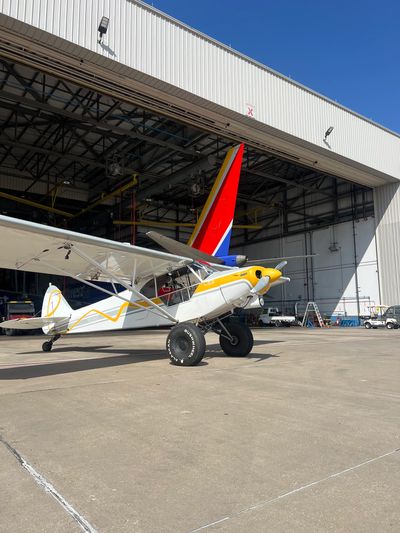 Small airplane parked outside a hangar under clear blue sky.