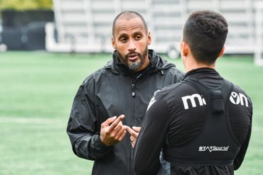 Two men in black sportswear engaged in conversation on a field.