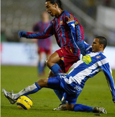 Soccer player in blue and white tackles an opponent in red and blue jersey.