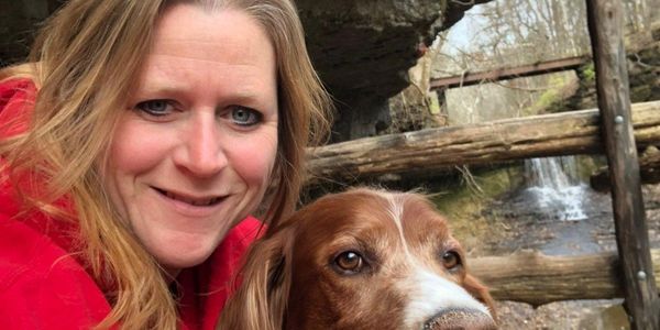 Woman and brown dog posing outdoors near a wooden fence.