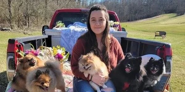 Woman sitting on truck bed with five small dogs.