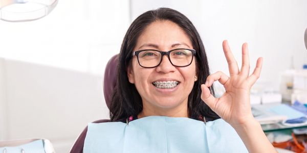 Woman with braces smiling and giving an OK sign at the dentist.