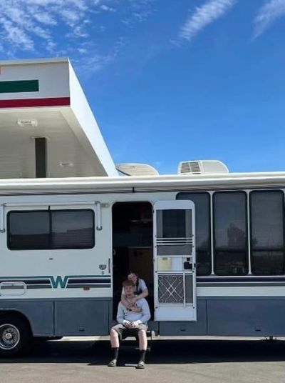 Two people sitting at the entrance of a parked RV under a clear sky.