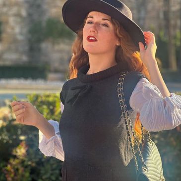 Woman in stylish black outfit and hat posing outdoors.