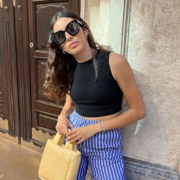 Woman in black crop top and striped pants holding a beige handbag.