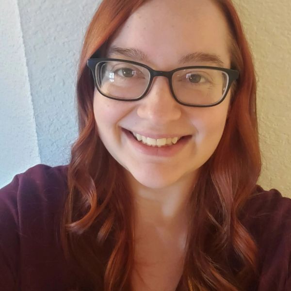 Smiling woman with glasses and red hair.