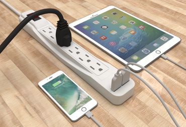 A power strip with multiple devices charging on a wooden floor.