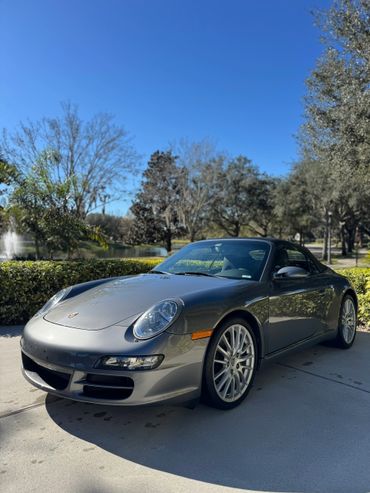 Silver Porsche convertible parked on a sunny day with clear blue sky.