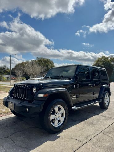 Black Jeep Wrangler parked under a partly cloudy sky.