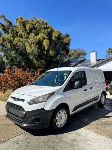 White Ford van parked on a sunny driveway with trees and a house in the background.