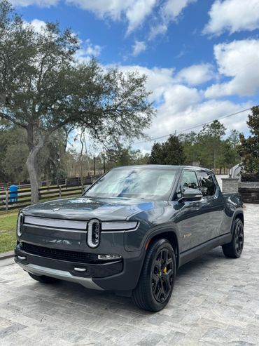 A sleek gray Rivian electric pickup truck parked on a stone driveway.