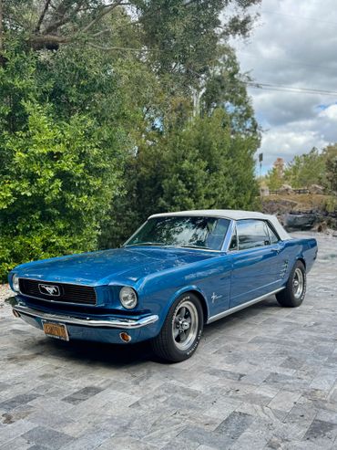 Blue classic Ford Mustang convertible with white top parked on a driveway.