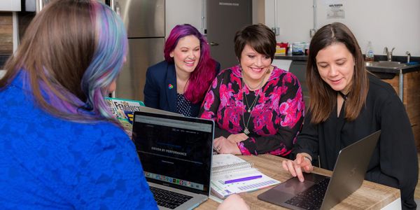Four women sitting at a desk looking at a computer during a meeting