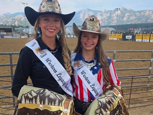 Two rodeo queens smiling wearing hats and sashes.