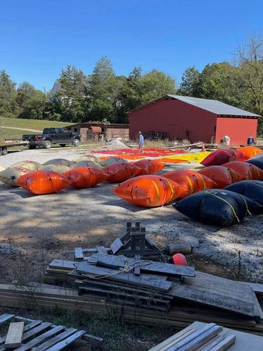 Large colorful inflatable sections laid out on gravel near red barns under a clear sky.