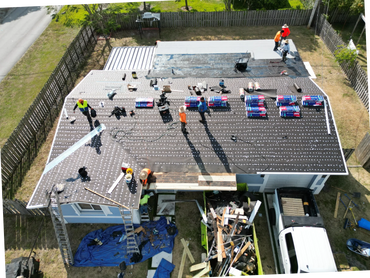 Workers installing a new roof on a house with materials and tools scattered around.