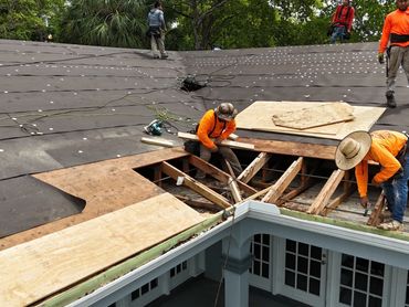 Workers repairing a roof with wooden planks and tools.