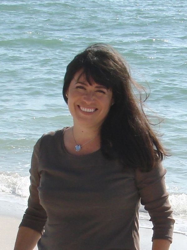 Cynthia smiling as she stands on the beach with the Gulf of Mexico behind her.