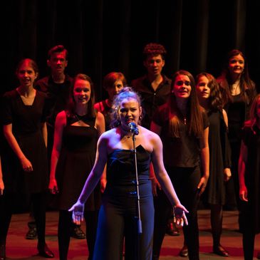 This is a picture of a female youth, solo singer with an ensemble of singers behind her.