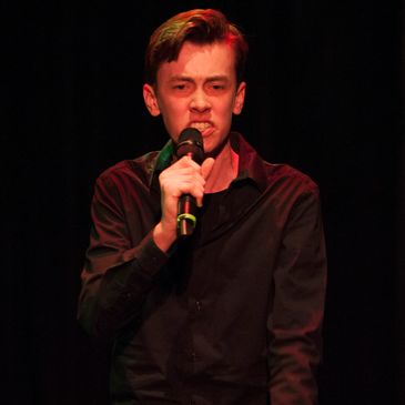 This is a picture of a young man singing at a concert into a cordless microphone.