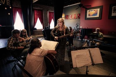 Ashlee is addressing a students question. She is facing the student and she is demonstrating somethiAshlee is addressing a students question. She is facing the student and she is demonstrating something on her guitar.