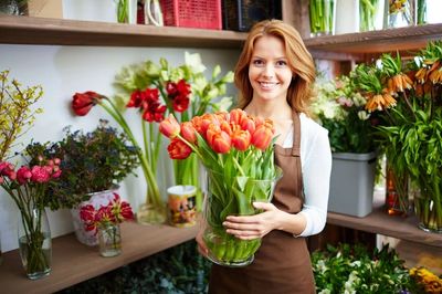 Smiling florist holding a vase of orange tulips.