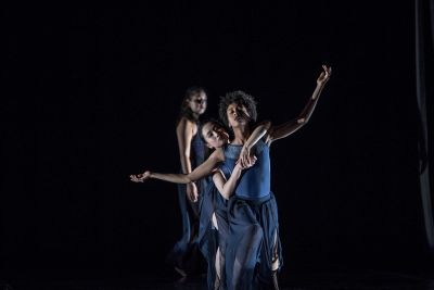 Three dancers perform on a dark stage.