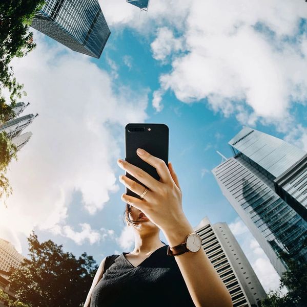Person taking a selfie with skyscrapers and blue sky.