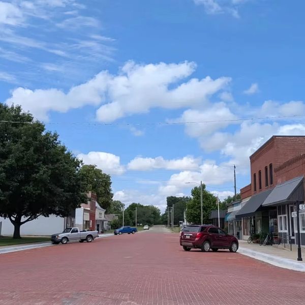 Quiet small-town street with brick pavement and parked cars.