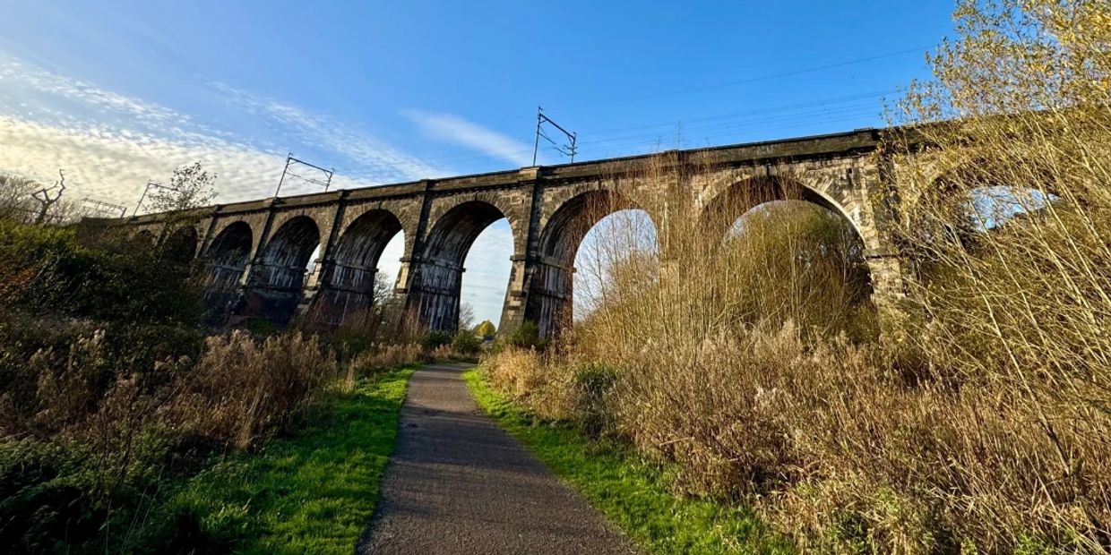 Stone railway viaduct over a nature path on a sunny day.
