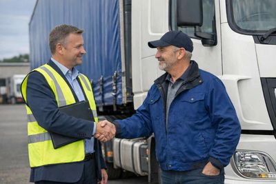 Two men shaking hands near a truck, one in a safety vest and the other in a blue jacket.