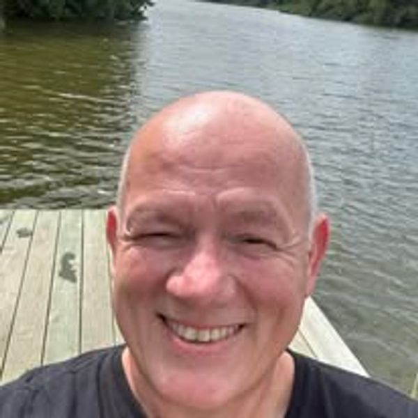 Smiling man enjoying a sunny day by the water on a wooden dock.