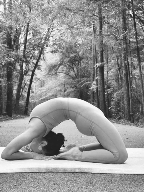 Person practicing advanced yoga pose on a mat outdoors in a forest.