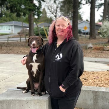 Woman with black hoodie posing with a brown dog outdoors.