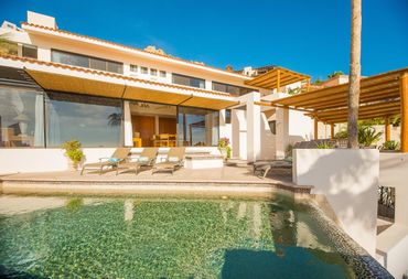 Sunny modern villa with pool and lounge chairs under clear blue sky.
