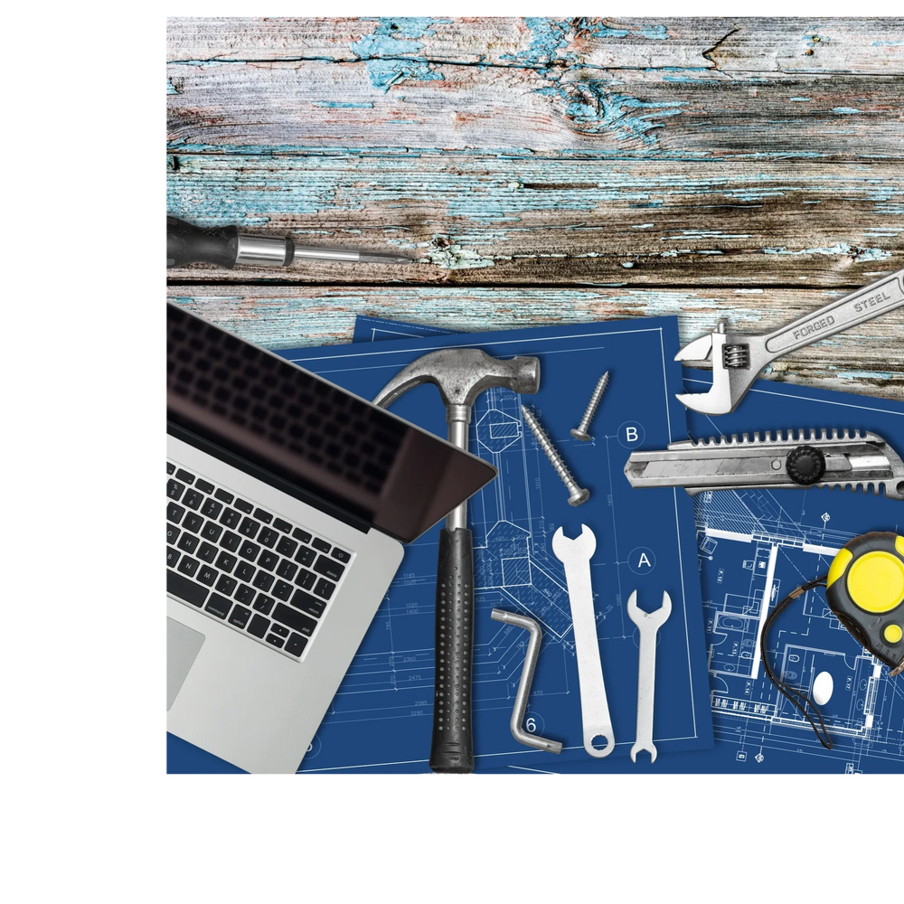 Laptop and various tools on blueprints on a rustic wooden table.