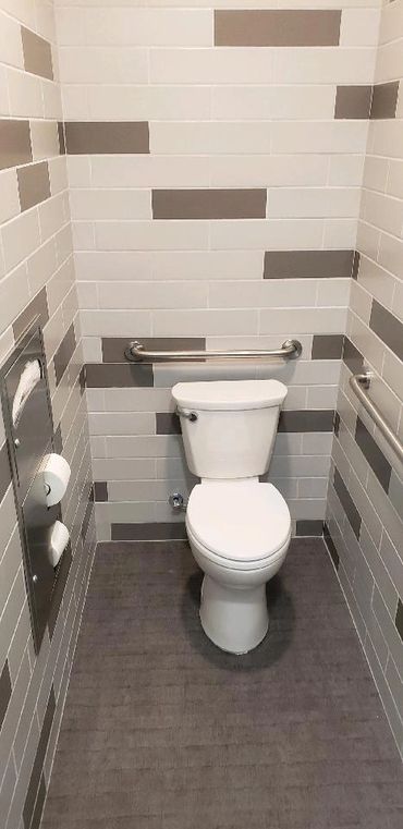 Clean, accessible restroom with a white toilet and grey tiled walls.