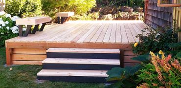Newly built wooden deck with steps and bench seating in a garden.