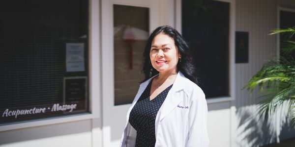 Smiling woman in a white medical coat standing outside.