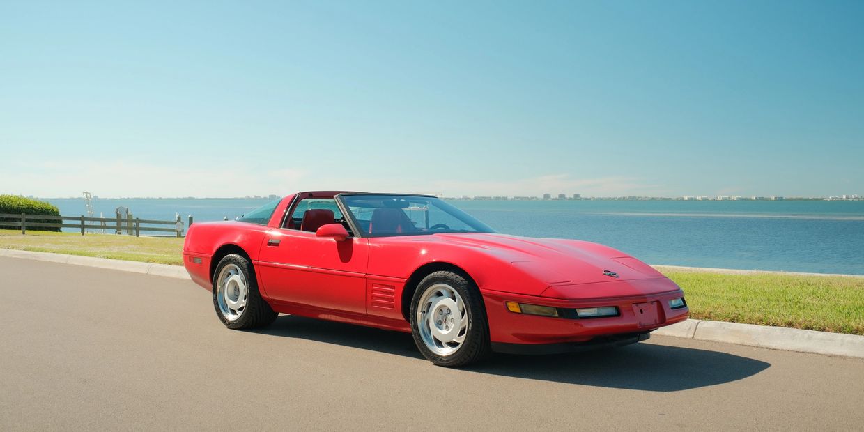 Red vintage sports car parked by the waterfront on a sunny day.