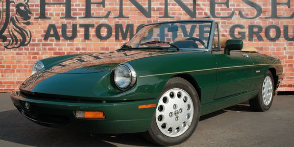 Green classic convertible sports car parked in front of a brick wall.
