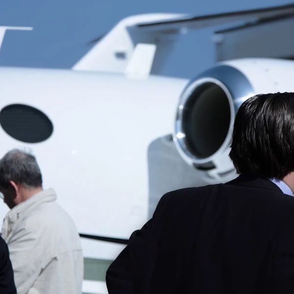 Two men near a private jet, one facing away.