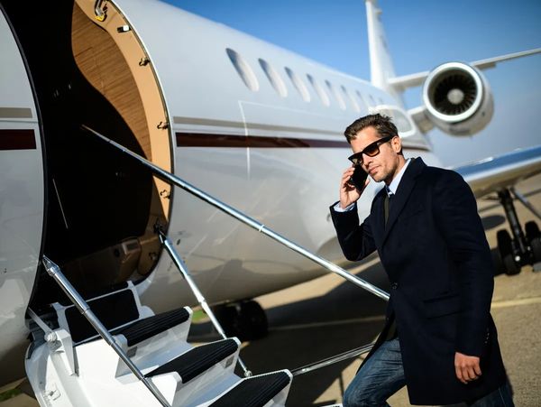Man in sunglasses talking on phone near private jet stairs.